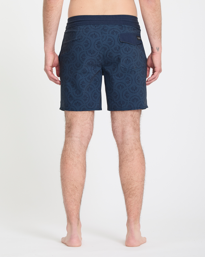 A person stands barefoot facing away, wearing Volcom Men's Psyche Cotton Stoney 17 swim shorts with a back pocket, on a white background.