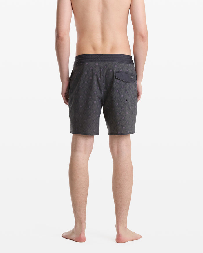 A shirtless person, barefoot and facing away, models the Volcom Men's Psyche Cotton Stoney 17 shorts, featuring a dark pattern, back pocket with a small label, all set against a plain white background.