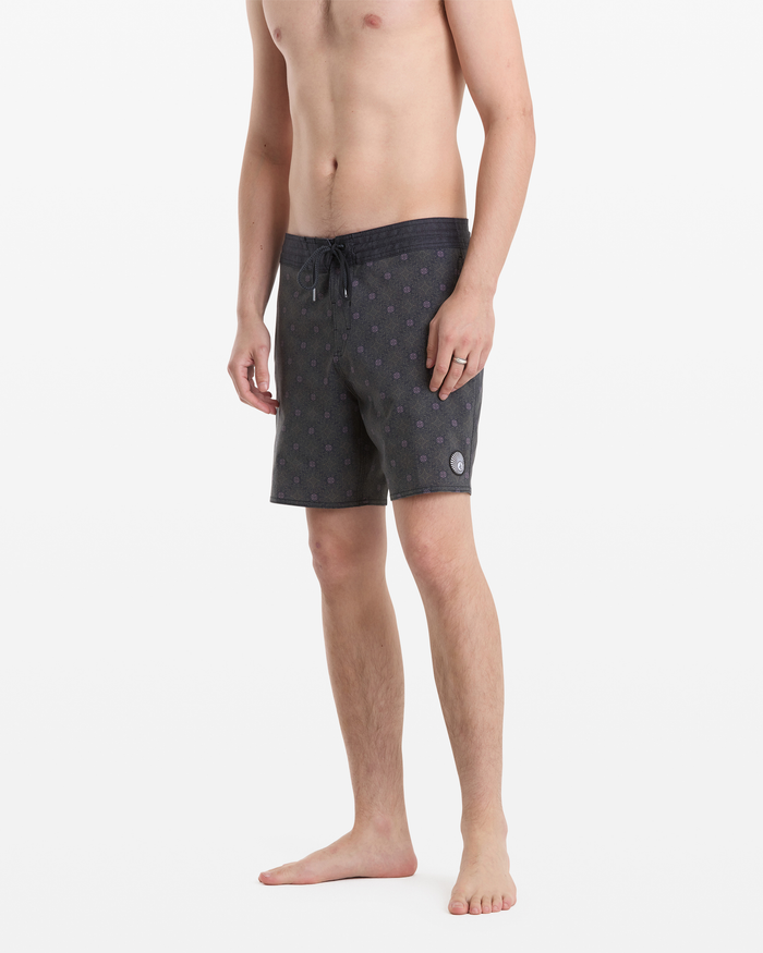 A shirtless man stands barefoot, wearing Volcom Men's Psyche Cotton Stoney 17 swim shorts with a subtle pattern and drawstring waist, facing slightly sideways against a plain white background.