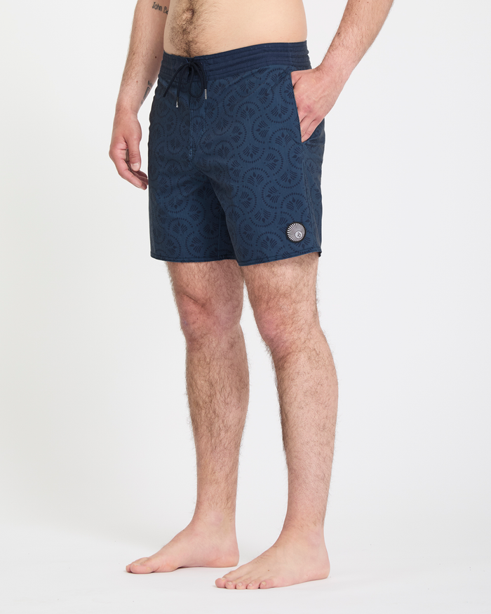 A barefoot man stands on a white background, hands in pockets, wearing Volcom Men's Psyche Cotton Stoney 17 navy patterned swim shorts with a drawstring waist. Only the lower half of his body is shown.