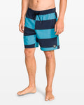 A person stands barefoot against a plain white background wearing Volcom Men's Psyche Cotton 17" Trunk swim shorts with a drawstring waist and side pocket.