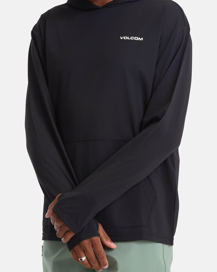 A man stands with arms crossed, hands partially covered by the sleeves of a black Volcom Men's Pullover Hood Long Sleeve and wearing green shorts.