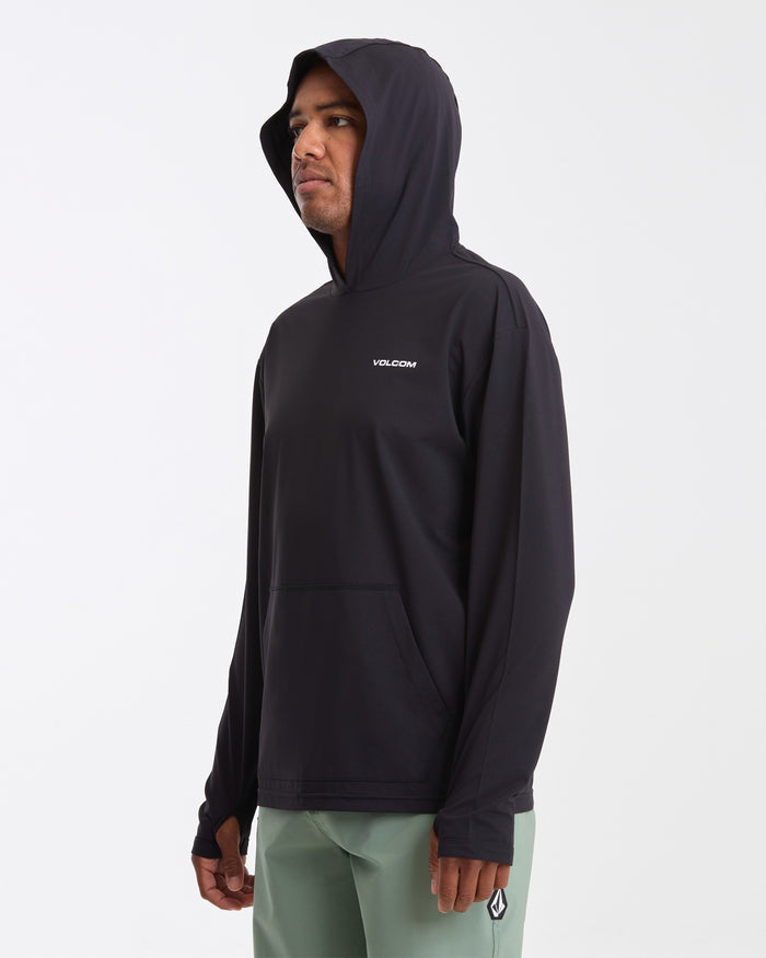 A man stands against a plain white background wearing a Volcom Men's Pullover Hood Long Sleeve with VOLCOM on the chest and light green pants.