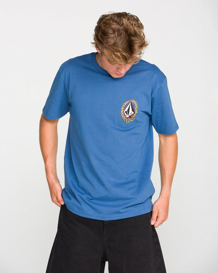 A person wearing the Volcom Men's Ringafire Short Sleeve Tee, crafted from premium ring spun cotton and adorned with a vibrant circular chest logo, looks down while standing against a plain white background.