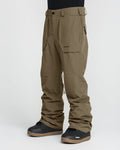 A person wearing Volcom Men’s Roan 20K Pants in olive green with black boots, standing against a plain white background. These pants are crafted from recycled fabric, feature convenient pockets, and display the VOLCOM logo on the upper thigh.