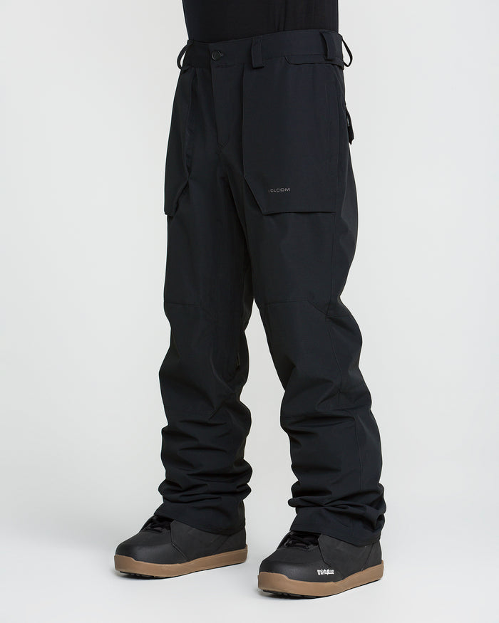 A person is wearing black Volcom Men’s Roan 20K Pants and black winter boots, standing against a plain white background. Only the lower half of the body is visible.