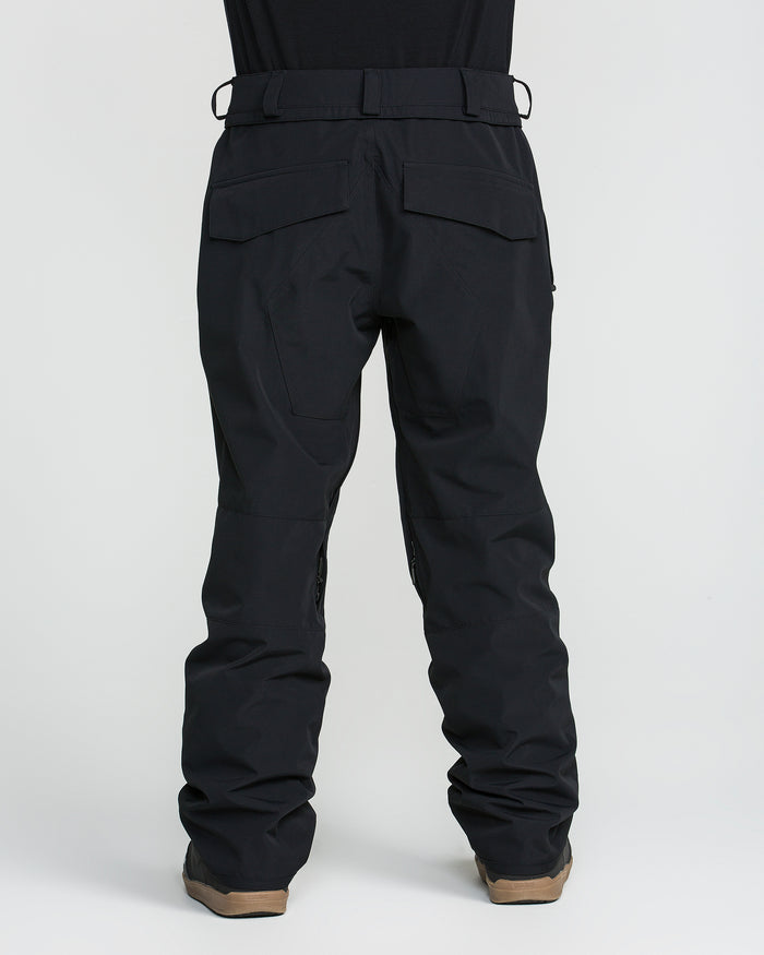 A person shown from the back against a plain white background is wearing Volcom Men’s Roan 20K Pants in black and brown shoes.