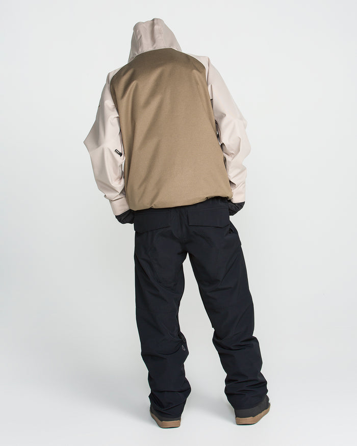 A person stands facing away, wearing a beige and tan hooded jacket paired with Volcom Men’s Roan 20K Pants in black and brown shoes, set against a plain white background.