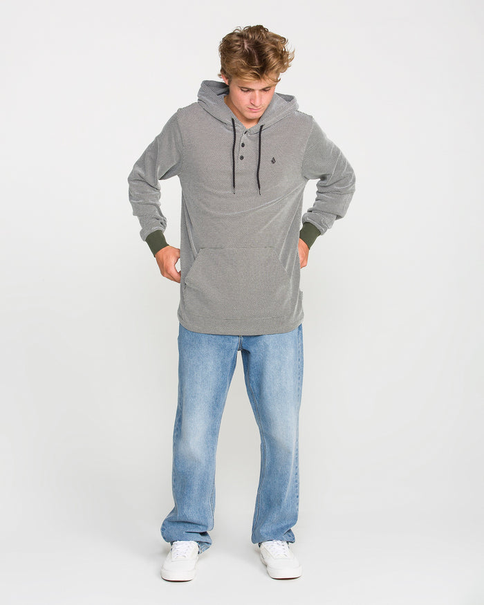 A person wearing the Volcom Men's Rowan Thermal Long Sleeve Shirt in gray stripes, paired with light blue jeans and white sneakers, stands against a plain white background, looking down with hands on their hips.