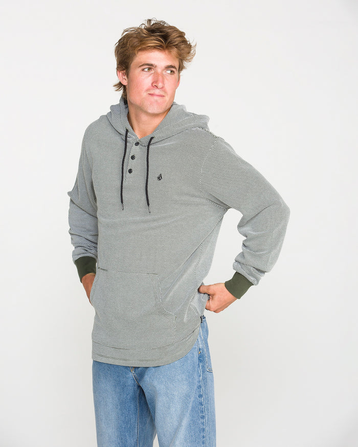 A person wearing the Volcom Men's Rowan Thermal Long Sleeve Shirt in gray, styled with blue jeans, stands with one hand on their hip and looks off to the side against a plain white background.