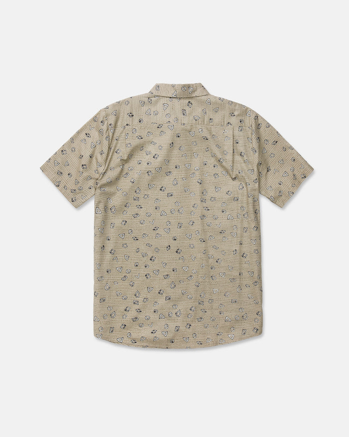A beige Men's Scaler Stone Short Sleeve Shirt by Volcom, featuring a classic fit and subtle dotted pattern with small black illustrated designs, made from a soft cotton-viscose blend and displayed from the back against a plain white background.