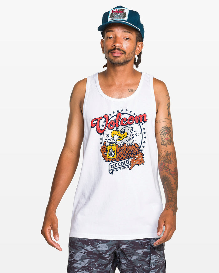A man in a blue hat and patterned shorts models the Volcom Men's Serve Stoked Tank, featuring a colorful eagle graphic, from the Froth of July collection, standing against a plain white background.