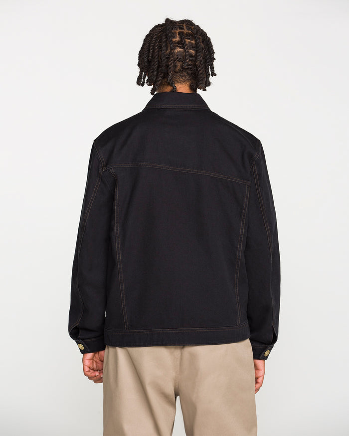 A person with short, twisted braids is shown from the back, wearing the Volcom Men's Slakers Jacket in black cotton canvas with visible seam lines and tan pants against a plain white background.