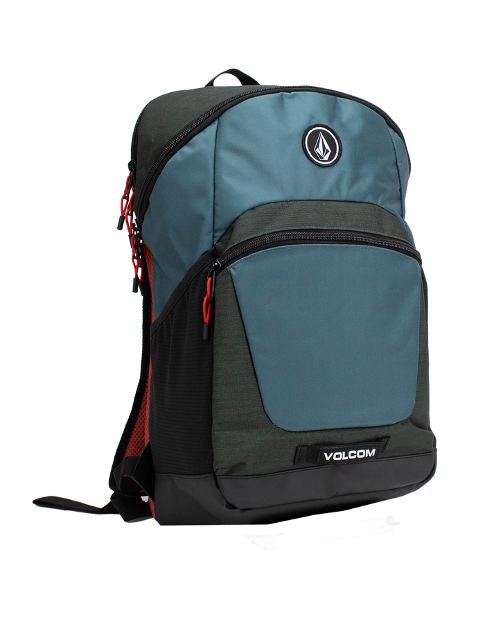 The Volcom Men's Slam School Backpack, shown in blue and black with red zipper pulls, features a front zip pocket, a large main compartment with a padded laptop sleeve, and a side mesh pocket, displayed standing upright on a white background.
