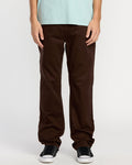 A person wears Volcom Men's Solver 5 Pocket Slub Pants and black sneakers with white soles, standing against a plain white background. Only their lower torso and legs are visible.