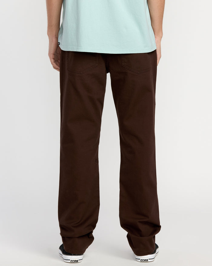A person stands facing away, wearing a light blue T-shirt, Volcom Men's Solver 5 Pocket Slub Pants, and white Converse sneakers against a white background.