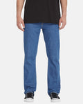 A person wearing a black t-shirt, Volcom Men's Solver Denim Pants in blue, and black-and-white sneakers, shown from the shoulders down against a plain white background.