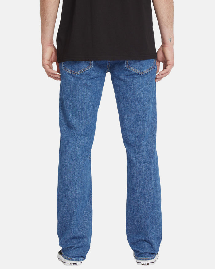 A person wearing a black shirt, Volcom Men's Solver Denim Pants, and white sneakers stands with their back to a plain white background, highlighting the Water Aware sustainable style.