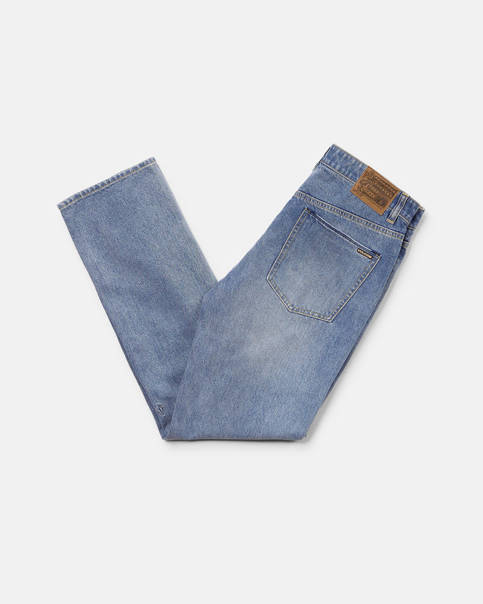 A pair of Volcom Men's Solver Denim Pants in Freedom Blue stretch denim, folded in half to display the back pocket and brown leather patch, highlights their modern straight leg cut against a plain white background.