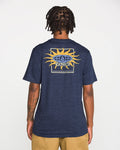 A person faces away, wearing the Volcom Men's Spf91 Short Sleeve Tee in navy blue, featuring a sun graphic and logo on the back. The medium-weight heather tee is paired with tan shorts, standing out against a plain white background.