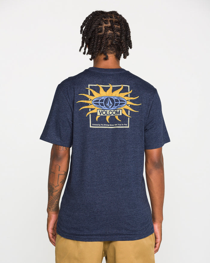 A person faces away, wearing the Volcom Men's Spf91 Short Sleeve Tee in navy blue, featuring a sun graphic and logo on the back. The medium-weight heather tee is paired with tan shorts, standing out against a plain white background.