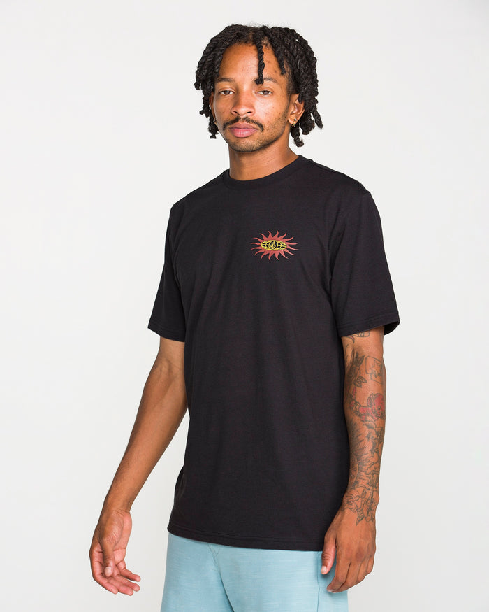 A man with short dreadlocks is wearing the Volcom Men's Spf91 Short Sleeve Tee in a black, medium-weight heather. The shirt features a small sun and eye graphic on the chest and is designed with a modern fit, crafted from a soft ring spun cotton-poly blend for everyday comfort. He stands against a plain white background.