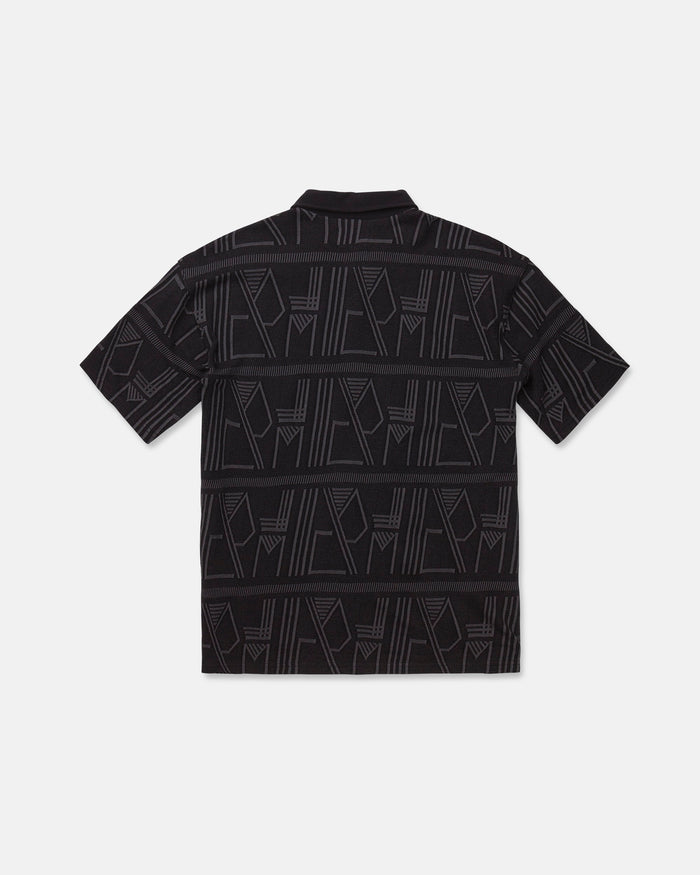 The Men's Stone Optix Polo by Volcom is a black short-sleeve shirt with an abstract geometric pattern in gray, featuring yarn-dyed jacquard lines and shapes across the fabric. Displayed flat to show the back side against a white background, this polo features a boxy fit.