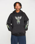 A person wearing the Volcom Men's Stone Trip Pullover in washed black, featuring white and green flame designs on the chest and sleeves, stands against a plain white background.
