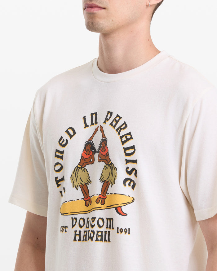 A man wears the Volcom Men's Stoned In Paradise Short Sleeve Tee, featuring two hula dancers on a surfboard and "Stoned in Paradise, Volcom Hawaii, Est 1991" text.