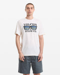 A man with short hair wears a white Volcom Men's Sunnies Short Sleeve Tee featuring a sunglasses graphic and dark gray shorts, standing against a plain white background.