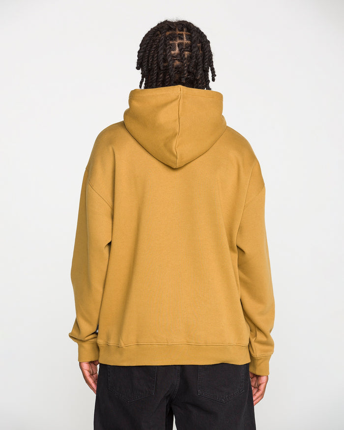 A person with braided hair, seen from behind, is wearing the Volcom Men's Super Stoned Pullover—a mustard yellow hoodie made from soft brushed-back fleece and recycled polyester—paired with black pants, standing against a plain white background.