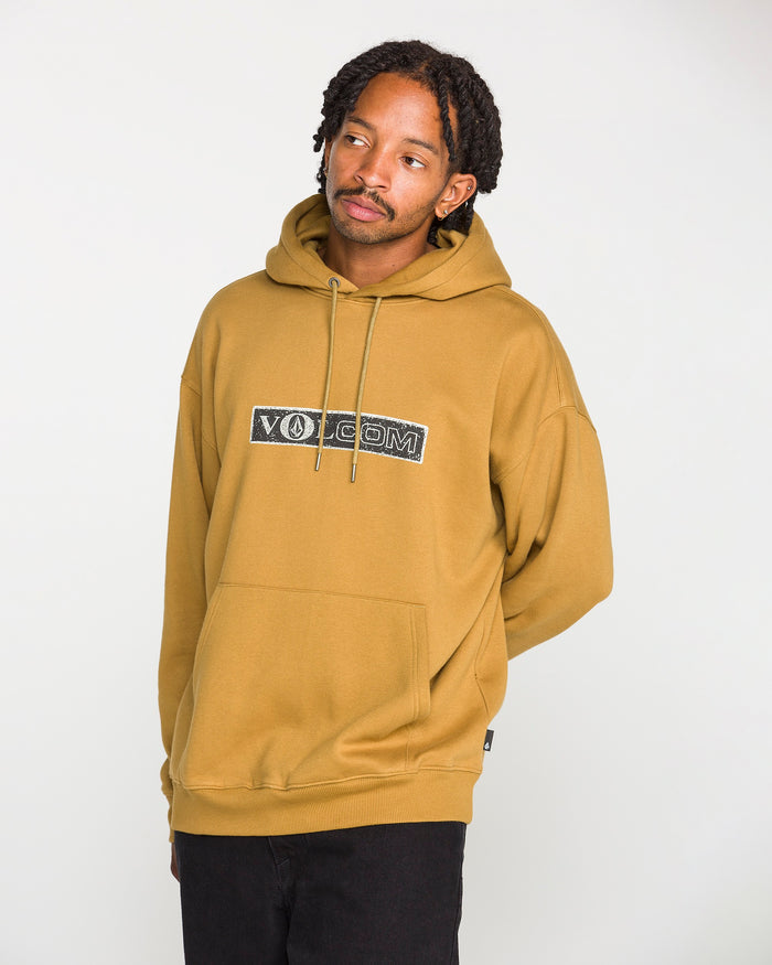 A man stands against a plain white background, looking slightly to the side, wearing the Volcom Men's Super Stoned Pullover in mustard yellow—crafted from soft brushed-back fleece with a front pocket—paired with black pants.