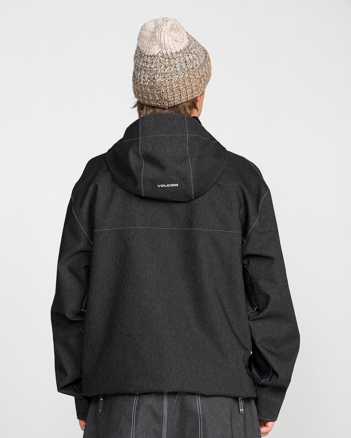 A person is shown from behind against a plain light background, wearing the Volcom Men’s Top Stitch Jacket— a black hooded 10K waterproof jacket with “VOLCOM” printed on the back— paired with a beige knit beanie.