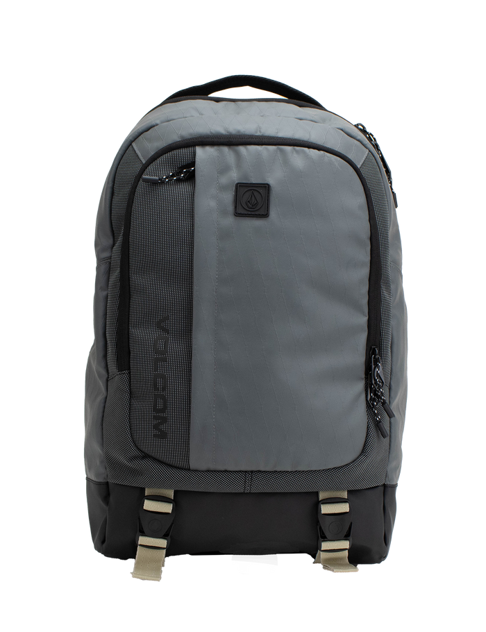 The Volcom Men's Venture Backpack features a gray design with a black bottom, front pocket, side zippers, and beige buckle straps. A small black logo patch accents the upper front. With a 22L capacity and padded laptop sleeve, this backpack offers a simple and functional style ideal for everyday use.