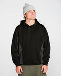 A person wearing a light gray beanie, olive green pants, and the Volcom Men’s Vital Hydro Pullover Hoodie in black with gray side panels stands against a plain white background, looking slightly upward and to the right.