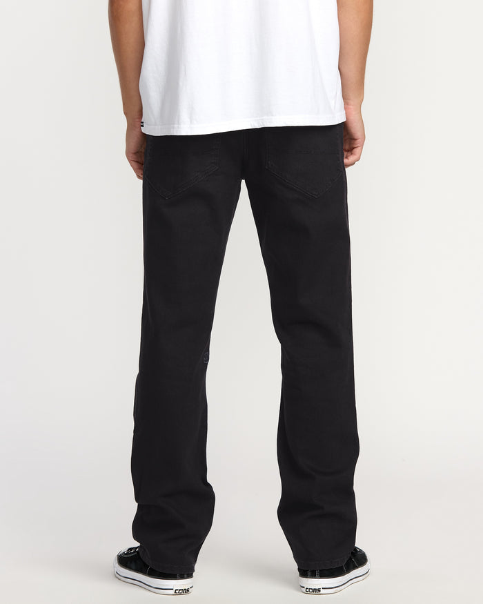 A person faces away, wearing a white T-shirt, black-and-white sneakers, and Volcom Men's Volcom Entertainment Pennywise Denim Pants, against a plain light backdrop.