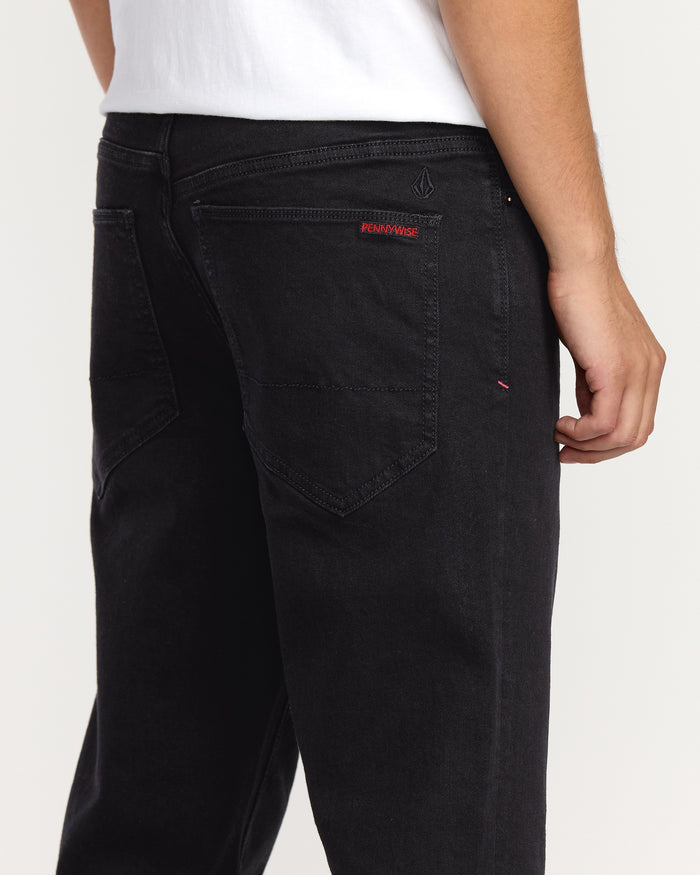A person wearing Volcom Men's Volcom Entertainment Pennywise Denim Pants, shown from the waist down and back. The black jeans have visible stitching and a small red Pennywise label above the right back pocket.