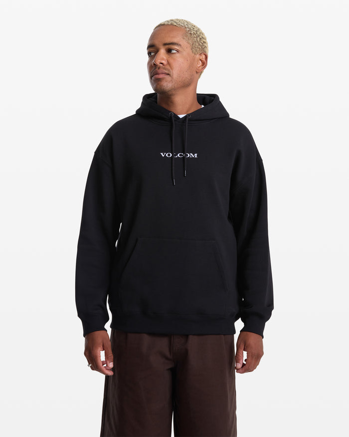 A man with short, light blond hair wears the Men's Volcom Stone Pullover by Volcom and brown pants, standing against a plain white background and looking slightly to the side.