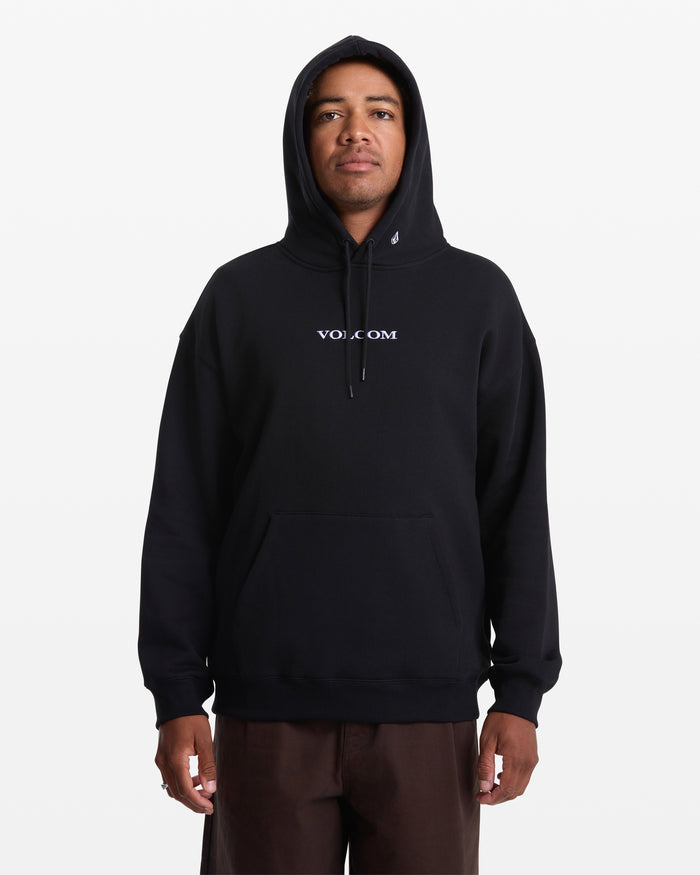 A person wearing the Men’s Volcom Stone Pullover by Volcom, a black BCI cotton fleece hoodie with “VOLCOM” in white on the chest, stands against a plain white background.