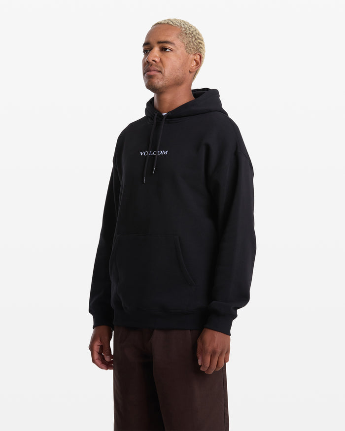 A man with short blonde hair wears the Men's Volcom Stone Pullover, a black fleece hoodie with "VOLCOM" on the front, paired with brown pants, standing against a white background.