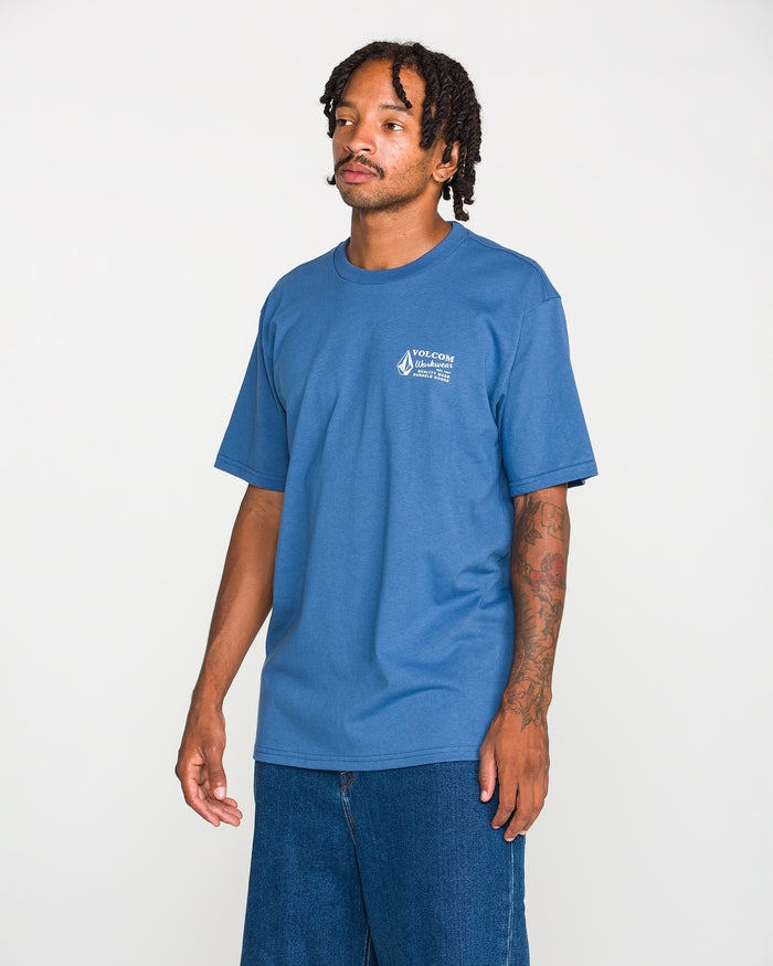 A man with tattoos and short dreadlocks wears the Volcom Men's Workwear Short Sleeve Tee paired with jeans, standing against a plain white background.