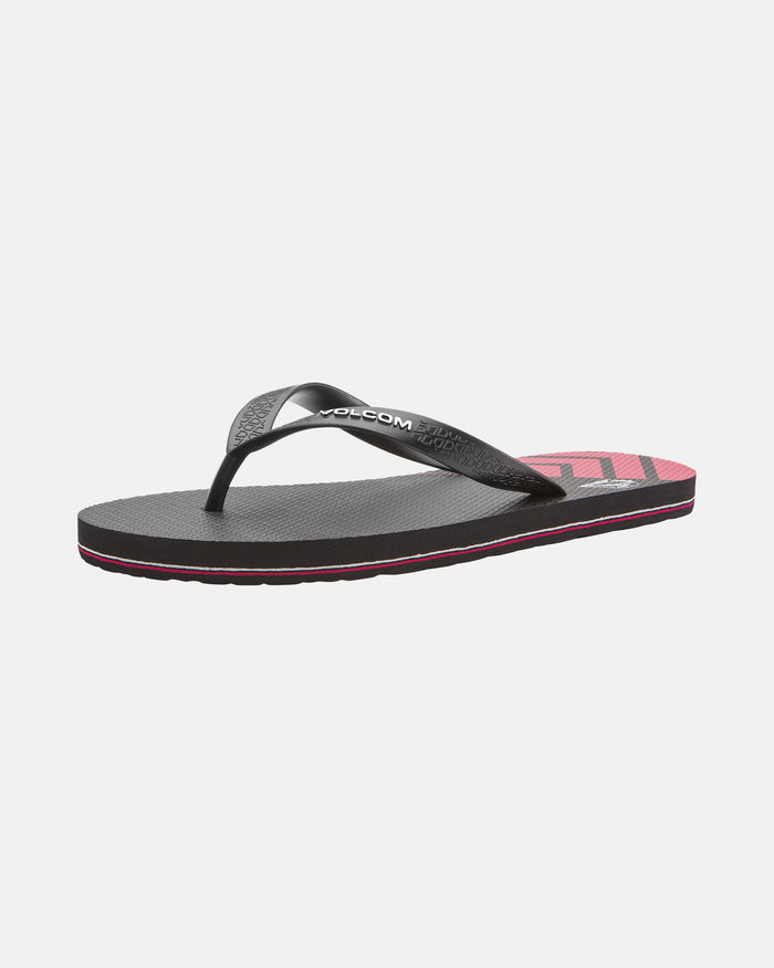 The Volcom Volcomotion Mens sandal features a black textured sole, black thong strap, pink and black insole design, thin pink midsole stripe, and bold VOLCOM branding. The flip-flop is showcased on a white background.