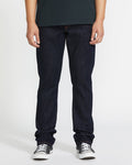 A person in a dark green T-shirt, Volcom Men's Vorta Denim slim fit jeans, and black-and-white sneakers stands against a plain white background. Their face is not visible.