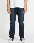 Wearing Volcom's Men's Vorta Denim jeans, a person stands against a plain white background. The image is cropped from the shoulders down and also shows a white t-shirt and black-and-white sneakers.