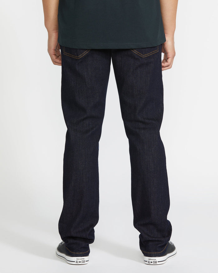A person in Volcom Men's Vorta Denim slim jeans, a dark shirt, and gray sneakers stands with their back to the camera against a plain white background.