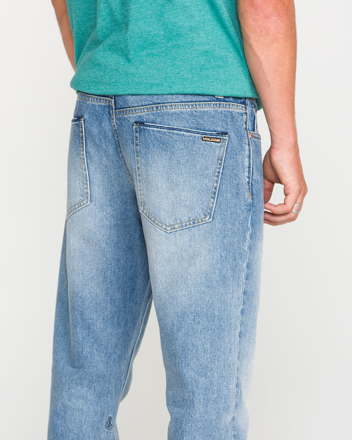 A person in a green shirt and light blue Volcom Men's Vorta Denim Pants is shown from the back, with one arm relaxed at their side. The Vorta denim features two back pockets and a small brand label above the right pocket.