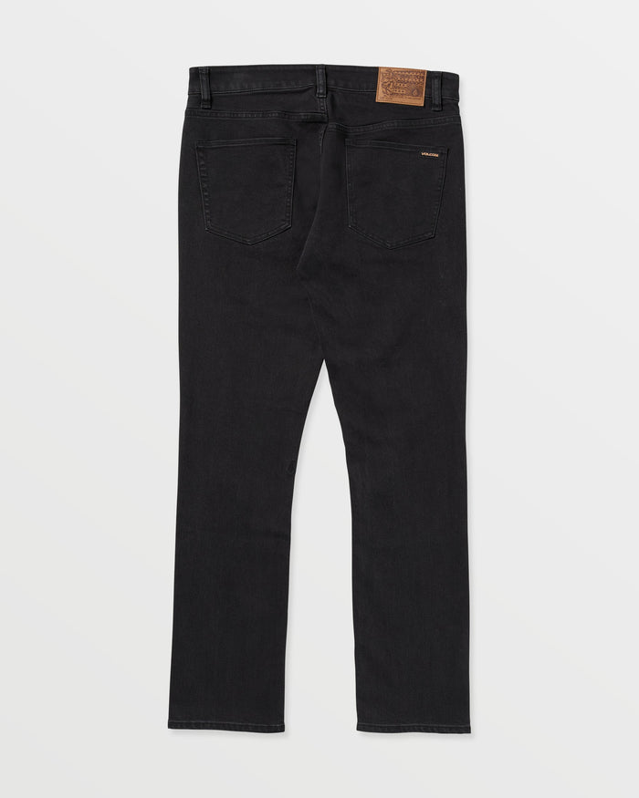 The Volcom Vorta Denim slim fit jeans in black are crafted from stretch denim, featuring two back pockets, belt loops, a brown leather patch on the waistband, and a sleek silhouette.