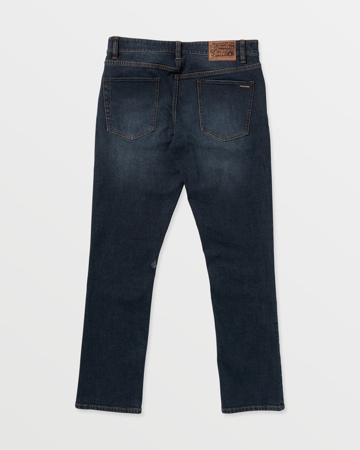 The Volcom Men's Vorta Denim jeans in dark blue are shown laid flat from the back on a white background. They feature two back pockets, brown stitching, a brown leather waistband patch, and straight-cut legs.