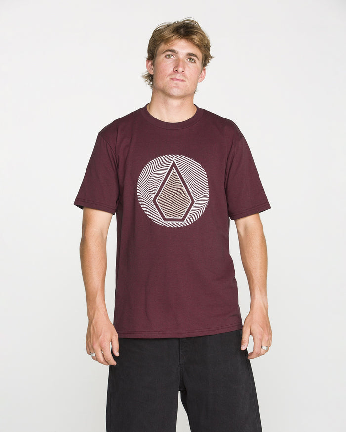 A man is wearing the Volcom Men's Wave Stone Short Sleeve Tee in burgundy, crafted from premium ring spun cotton and featuring the signature geometric Wave Stone design on the chest. He stands against a plain white background, facing the camera with a neutral expression.