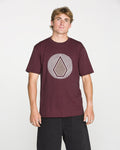 A man is wearing the Volcom Men's Wave Stone Short Sleeve Tee in burgundy, crafted from premium ring spun cotton and featuring the signature geometric Wave Stone design on the chest. He stands against a plain white background, facing the camera with a neutral expression.
